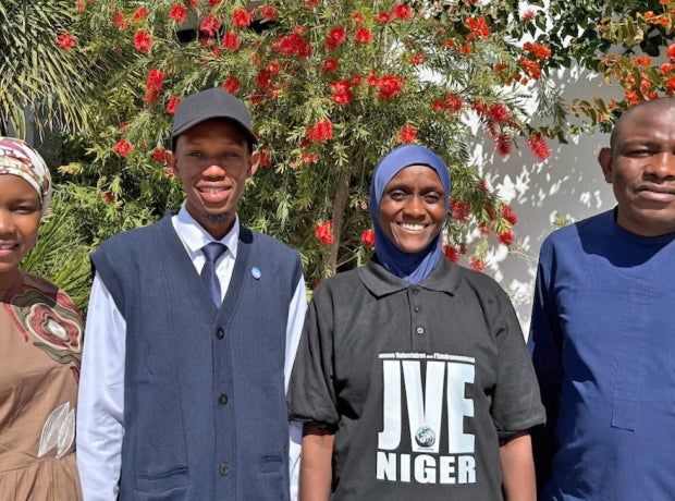 Four people in a group photo with vegetation behind